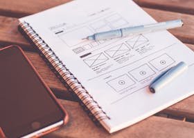 Close-up of a notebook with wireframe sketches and a smartphone on a wooden desk.