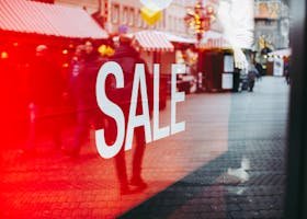 Red sale sign on storefront window reflecting a busy urban street scene, capturing city life.