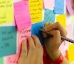Hands writing on colorful sticky notes during a brainstorming session indoors.