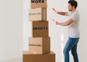 A man in casual attire balances boxes labeled with stress-related words indoors.